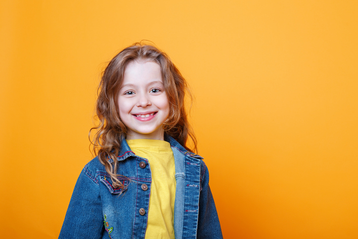 Portrait of beautiful happy little curly girl on orange background