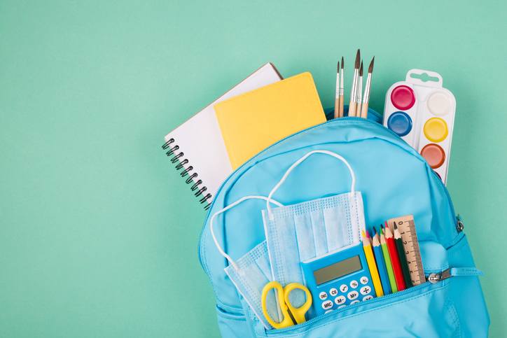 Healthcare concept. Studies during quarantine concept. Top above overhead view photo of backpack filled with colorful stationery and two blue masks isolated on turquoise background